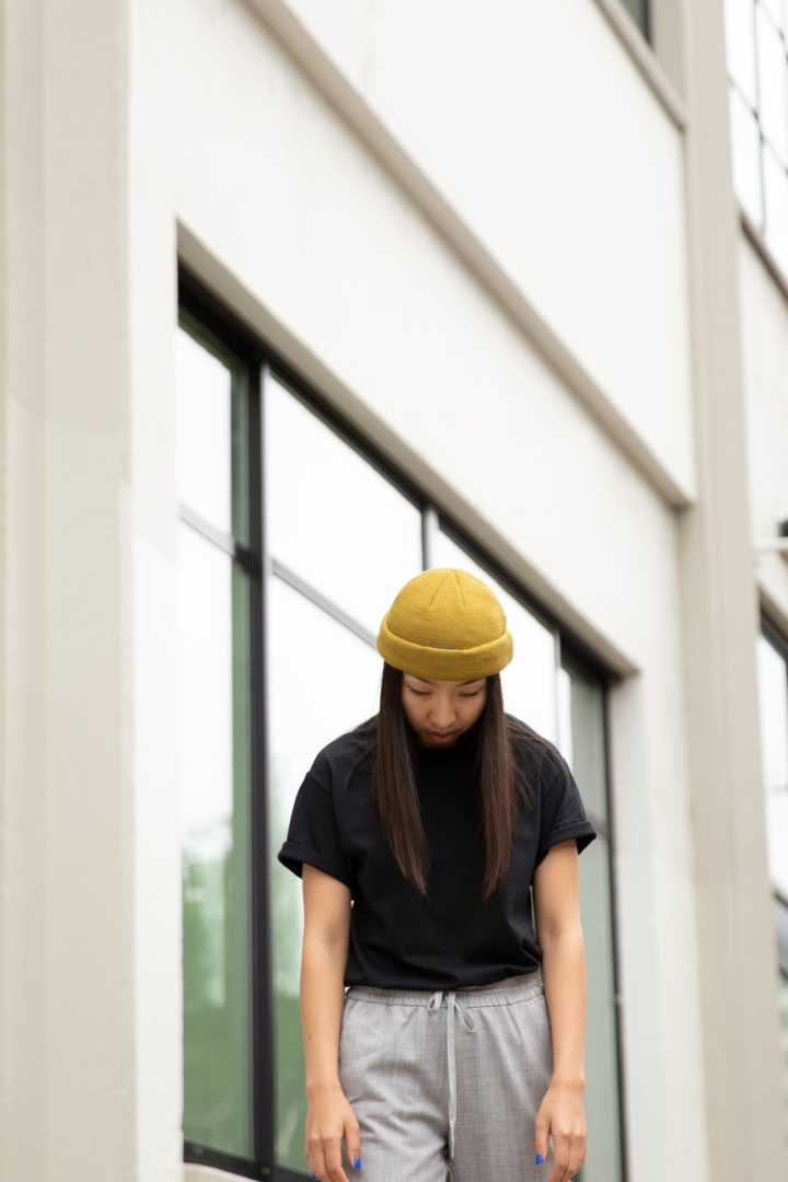 adult,asian model,beanie,black shirt,building,casual,city,contemporary,daylight,fashion,glass items,looking down,model,person,photoshoot,portrait,pose,reflection,urban,wall,wear,windows,woman