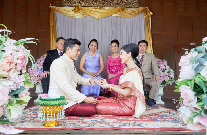 bride,groom,wearing,ring,finger,front,parents,sitting,smiling,together,male,female,man,woman,couple,love,family,relatives,husband,wife,group,six,people,bridal,guest,asia,asian,thai,thailand,thai style,traditional,vintage,religion,religious,dress,buddhist,buddhism,wedding,mariage,married,celebration,decoration,hand,congratulation,jasmine,flower,pot,sacred,happiness,elegent,beautiful,engagement,khan maak,betel bowl,xframe